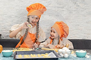 Happy family. Funny girls kids in orange chef uniform are preparing the dough, bake cookies in the kitchen. Sisters children enjoy