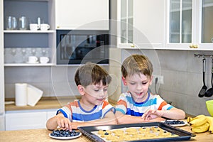 Happy family funny kids are preparing the dough, bake cookies in the kitchen. Put berry and blueberry in all biscuits