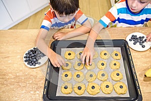 Happy family funny kids are preparing the dough, bake cookies in the kitchen. Put berry and blueberry in all biscuits