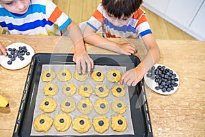 Happy family funny kids are preparing the dough, bake cookies in the kitchen. Put berry and blueberry in all biscuits