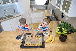 Happy family funny kids are preparing the dough, bake cookies in the kitchen. Put berry and blueberry in all biscuits