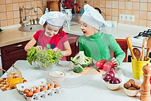 Happy family funny kids are preparing the a fresh vegetable salad in the kitchen