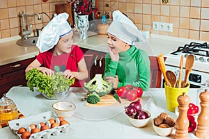 Happy family funny kids are preparing the a fresh vegetable salad in the kitchen