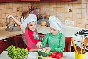 Happy family funny kids are preparing the a fresh vegetable salad in the kitchen