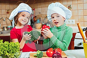 Happy family funny kids are preparing the a fresh vegetable salad in the kitchen