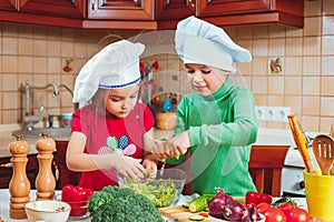 Happy family funny kids are preparing the a fresh vegetable salad in the kitchen