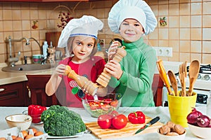 Happy family funny kids are preparing the a fresh vegetable salad in the kitchen