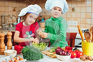 Happy family funny kids are preparing the a fresh vegetable salad in the kitchen