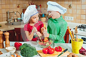 Happy family funny kids are preparing the a fresh vegetable salad in the kitchen