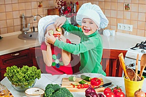 Happy family funny kids are preparing the a fresh vegetable salad in the kitchen