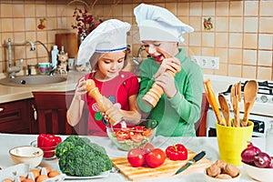 Happy family funny kids are preparing the a fresh vegetable salad in the kitchen