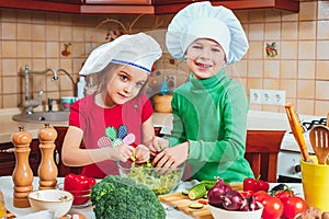 Happy family funny kids are preparing the a fresh vegetable salad in the kitchen