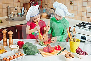Happy family funny kids are preparing the a fresh vegetable salad in the kitchen