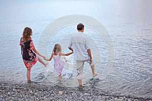 Happy family with girl on beach go in water