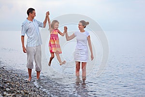 Happy family with girl on beach, parents lift girl