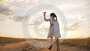 A happy family. A girl in a dress with a paper airplane in her hands runs across a wheat field. The kid plays an aviator