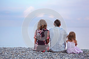 Happy family with girl sitting on beach, by back