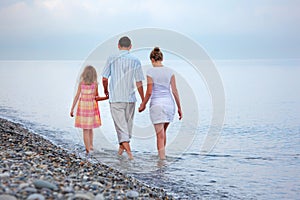 Happy family with girl walk on beach in evening