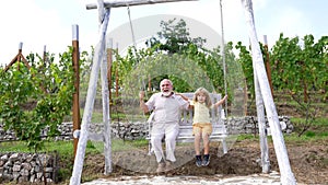 Happy family of grandad and grandson child swing together in backyard, swinging