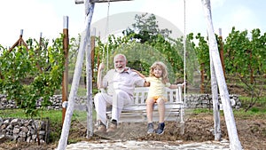 Happy family of grandchild and grandfather enjoy swinging together in backyard, swing