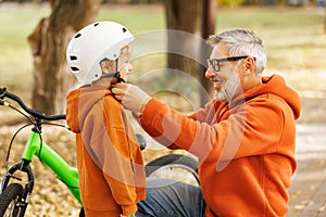 Happy family grandfather puts on grandson helmet for safe cycling in park