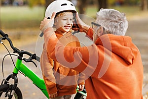 Happy family grandfather puts on grandson helmet for safe cycling in park