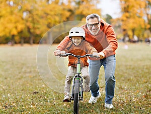 Happy family grandfather teaches child grandson  to ride a bike in park