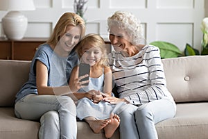 Happy family of grandmother, mother and daughter using cellphone together