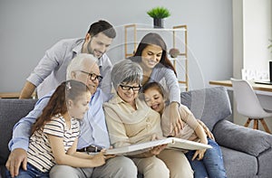 Happy family grandparents with twin granddaughters and their parents browse the family photo album.