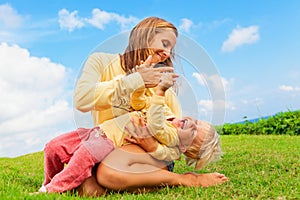 Mother tickling funny baby son lying on her laps