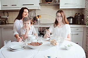 Happy family having breakfast at home. Mother with two kids eating in the morning in modern white kitchen