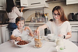 Happy family having breakfast at home. Mother with two kids eating in the morning in modern white kitchen