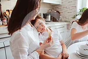 Happy family having breakfast at home. Mother with two kids eating in the morning in modern white kitchen