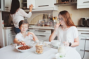 Happy family having breakfast at home. Mother with two kids eating in the morning in modern white kitchen