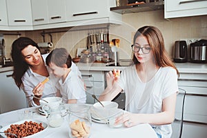 Happy family having breakfast at home. Mother with two kids eating in the morning in modern white kitchen