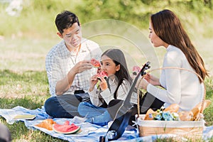 Happy family having enjoying outdoor sitting on picnic blanket eating watermelon in park sunny time