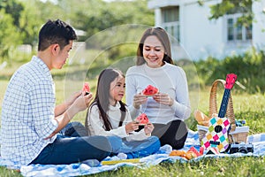 Happy family having enjoying outdoor sitting on picnic blanket eating watermelon in park sunny time