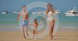 Happy family having fun on the beach. Mom running along the beach with her teenage son and little daughter