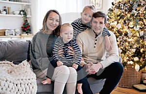 Happy family having fun in bedroom. Cheerful young family with kids sitting on sofa, embracing and laughing