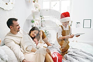 Happy family having fun on digital tablet in bed on Christmas