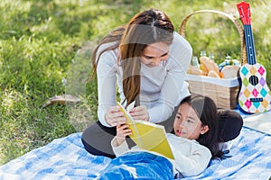 Happy family having fun and enjoying outdoor laying on picnic blanket reading book