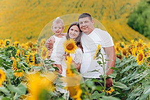 Happy family having fun in the field of sunflowers. Mother holding her daughter and sunflower in hand. The concept of summer