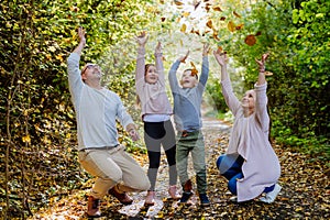 Happy family having fun with a foliage in autumn forest.