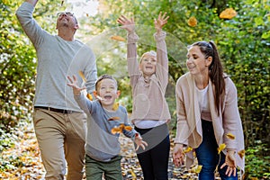 Happy family having fun with a foliage in autumn forest.