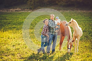 Happy family having fun with horses outdoors on green field on summer day