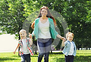 Happy family is having fun, mother playing with two children sons running on the grass in summer park on a sunny day