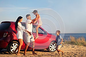 Happy family having fun near car on sandy beach. Summer trip
