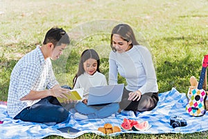 Happy family having fun outdoor on picnic using laptop computer technologies relaxing to open song