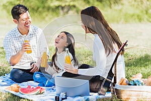 Happy family having fun outdoor sitting on picnic blanket drinking orange juice from glass bottle