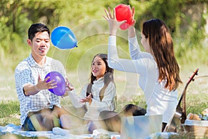 Happy family having fun outdoor sitting on picnic blanket playing balloons